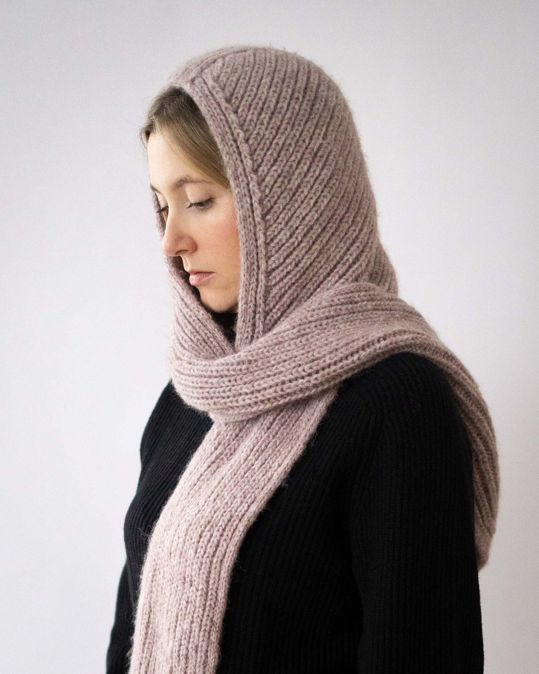 Person wearing a large knitted scarf on a plain background
