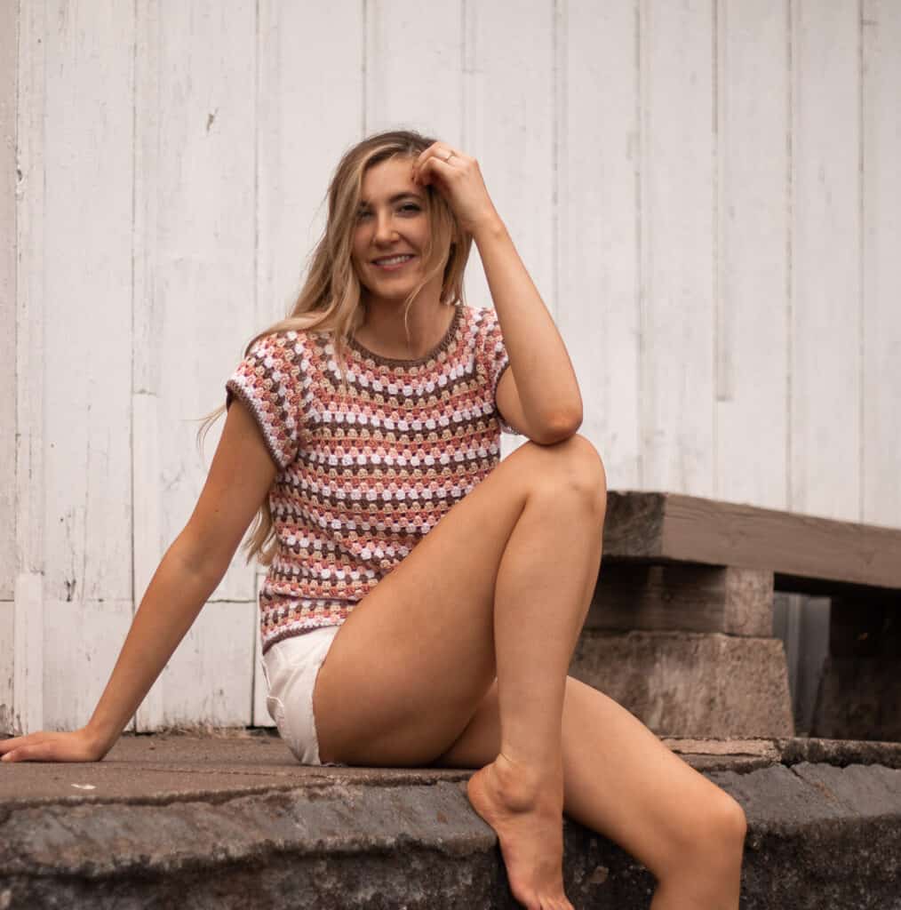 lifestyle image of maria top being worn on a model sitting on a sidewalk in front of white building smiling at the camera