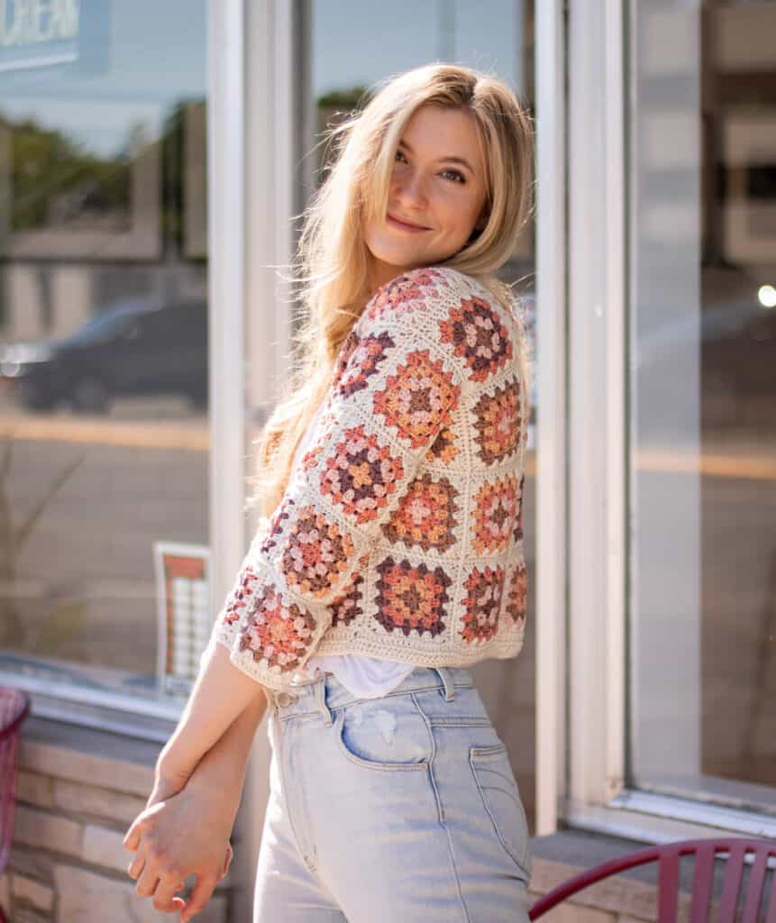 model wearing a multicolored crochet cardigan turning slightly to the side and smiling at the camera