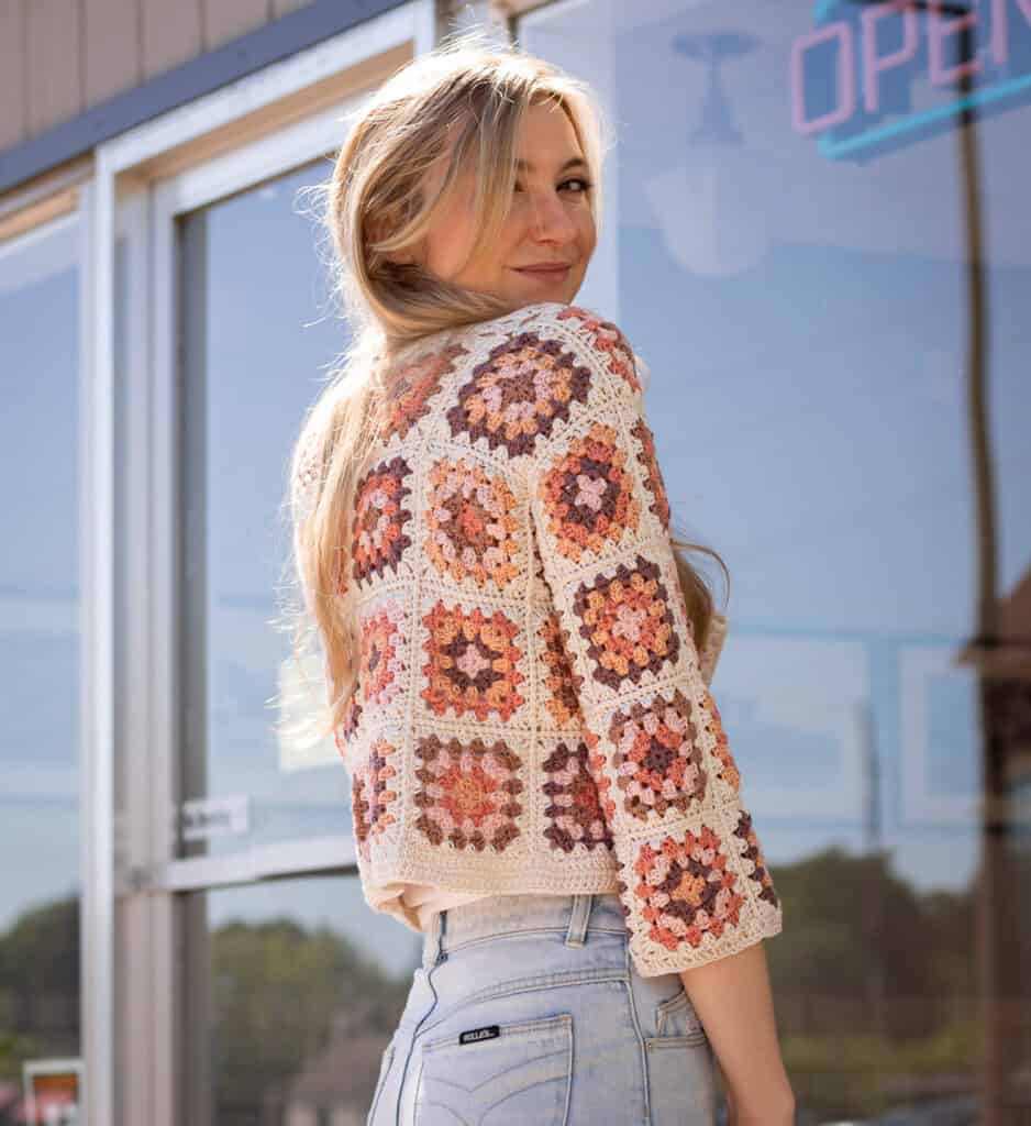 model wearing a colorful pink and orange crocheted cardigan turned to the back