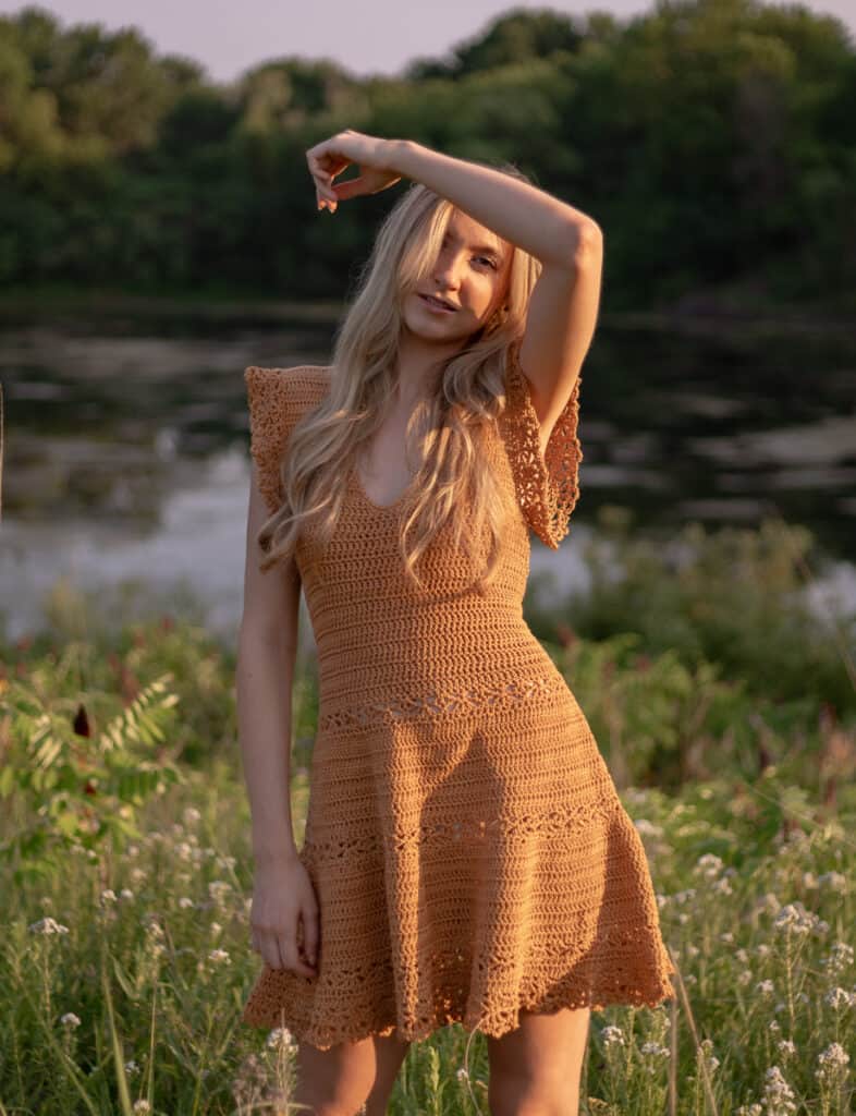 Chestnut orange crochet dress with a flowy tiered lace and flutter sleeves being worn by model with the sun shining brightly on her