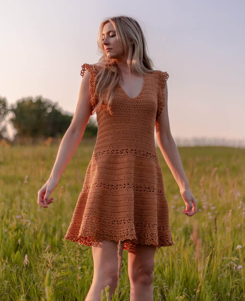 Crochet sun dress being worn in a field in late summer. Dress is amber colored with lace detailing and a flowy skirt