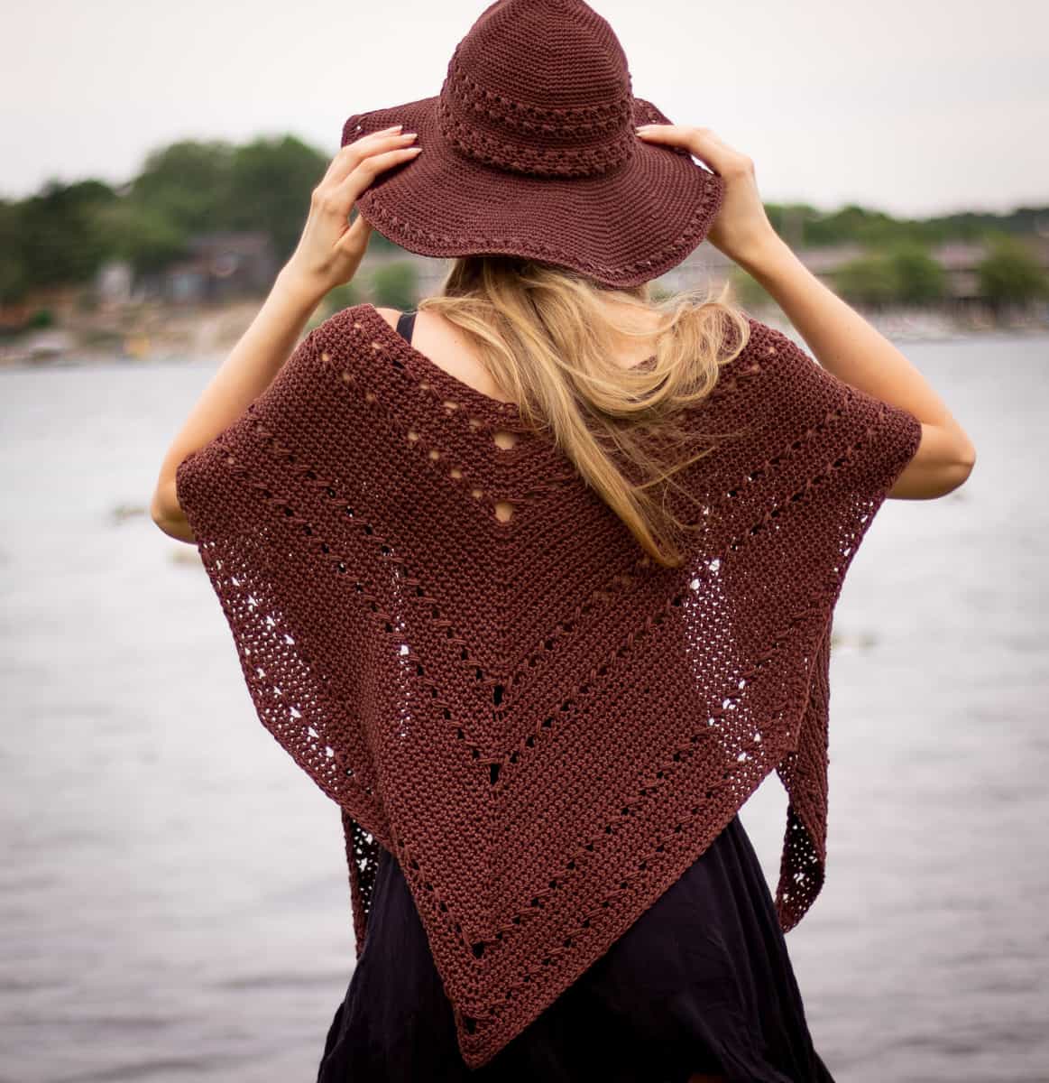 Seaside shawl being worn with the seaside sun hat in front of water. Model is wearing the shawl over her shoulders in a traditional style. This shawl is convertible and this is just one of the many ways to wear it