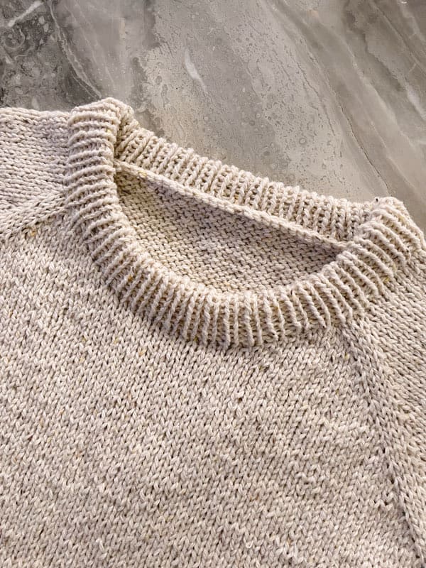Neckline detail of a top down raglan style sweater knitting pattern laying on top of a marble table.  The neckline in nicely curved and lower in the front for a comfortable fit.  