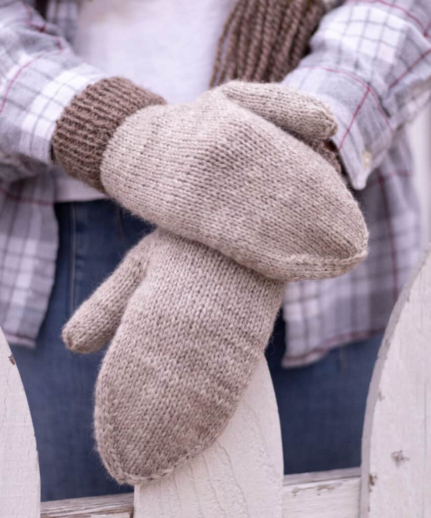 Detail image of the mittens showcasing the decreases at the fingers that shape the hand for a perfect fit. Mittens are show outside worn on hands that are holding onto a white fence.