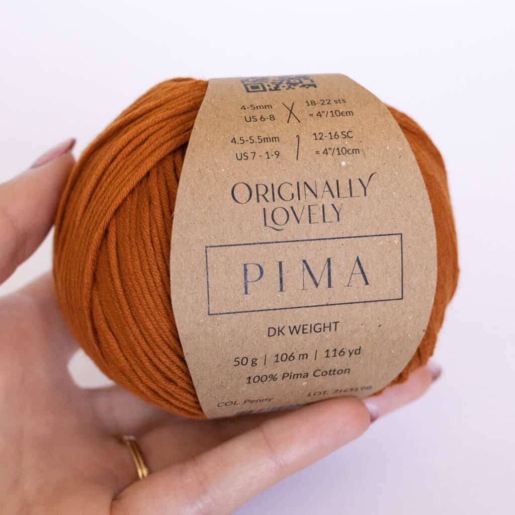 Pima yarn ball shown in the color Penny, held in a hand to show scale