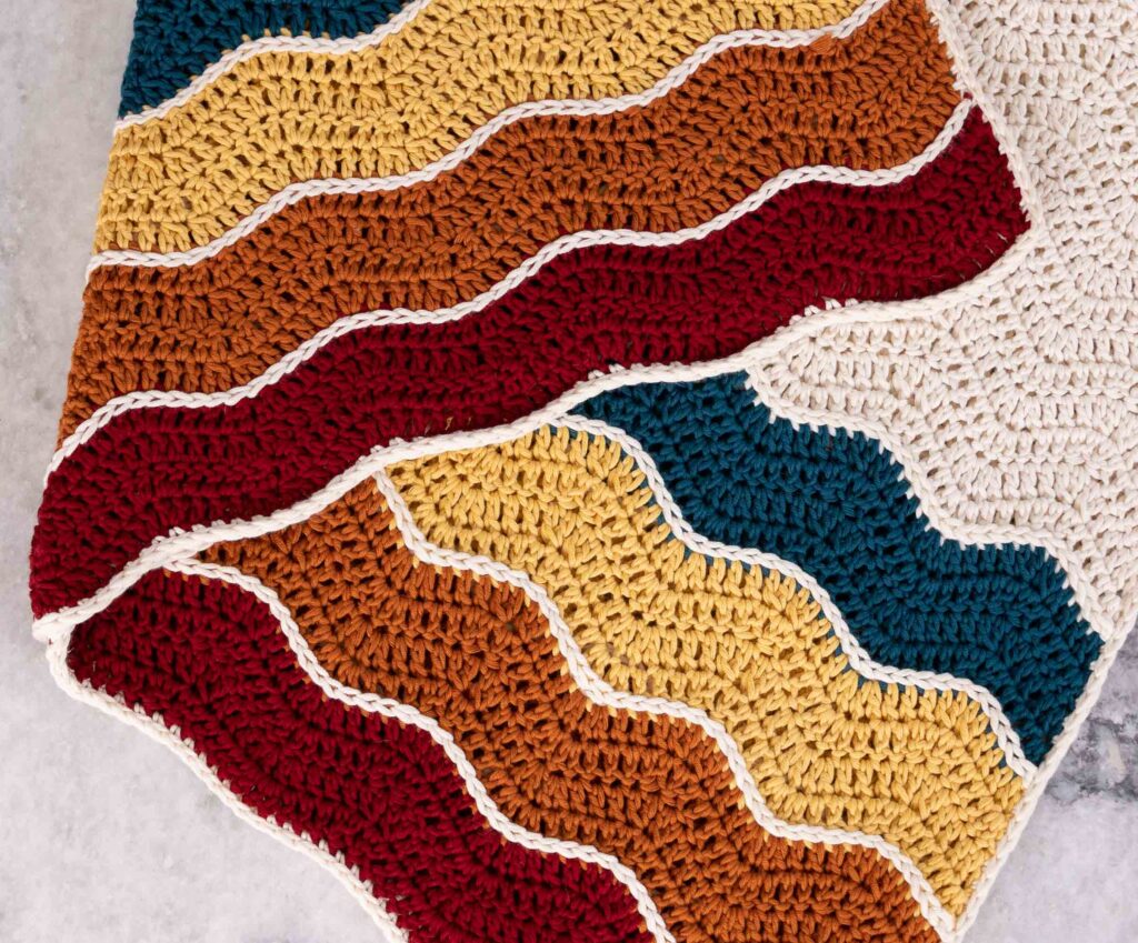 Wavy baby Blanket shown from above folder over on top of itself to showcase the stitch detailing and the vivid Pima yarn