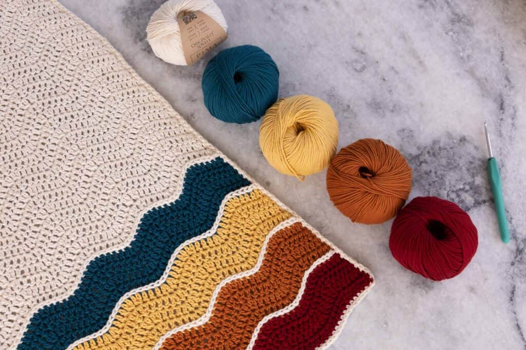 Vintage inspired baby blanket lined up showing the materials needed next to the blanket.  You will need Originally Lovely Pima yarn, a 4.5 mm crochet hook, and a tapestry needle to weave in your ends. 