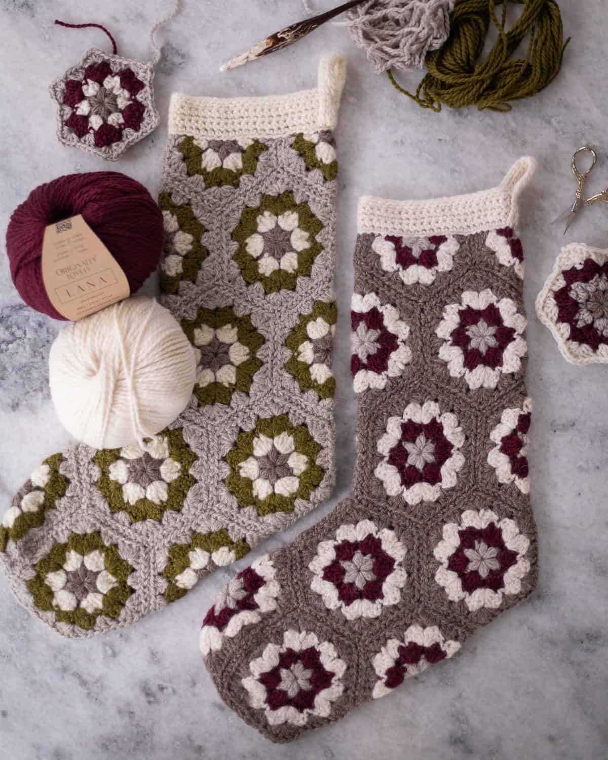 Granny Hexi Stocking Main Image shown with stockings laying flat on a table and the supplies used to make the Christmas stockings scattered around